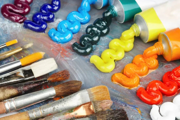 A collection of used paintbrushes and colorful acrylic paint tubes squeezed onto a palette, showcasing a vibrant mix of artistic tools and materials.